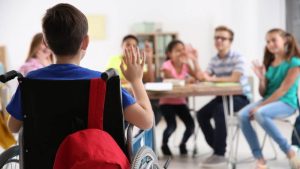 Kid with an IEP sits in a wheelchair and waives at classmates