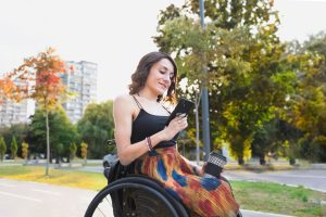 Woman using a wheelchair, checks her phone outside
