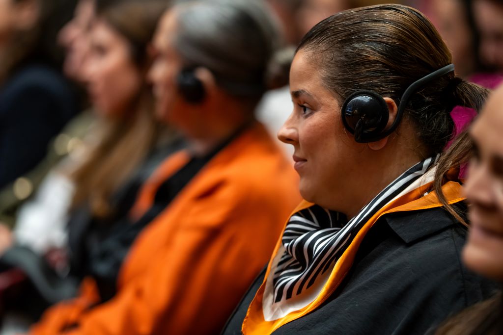 Woman attending conference listens wearing headphones.