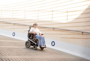 Woman takes a ramp to a lower level using a using a motorized wheelchair