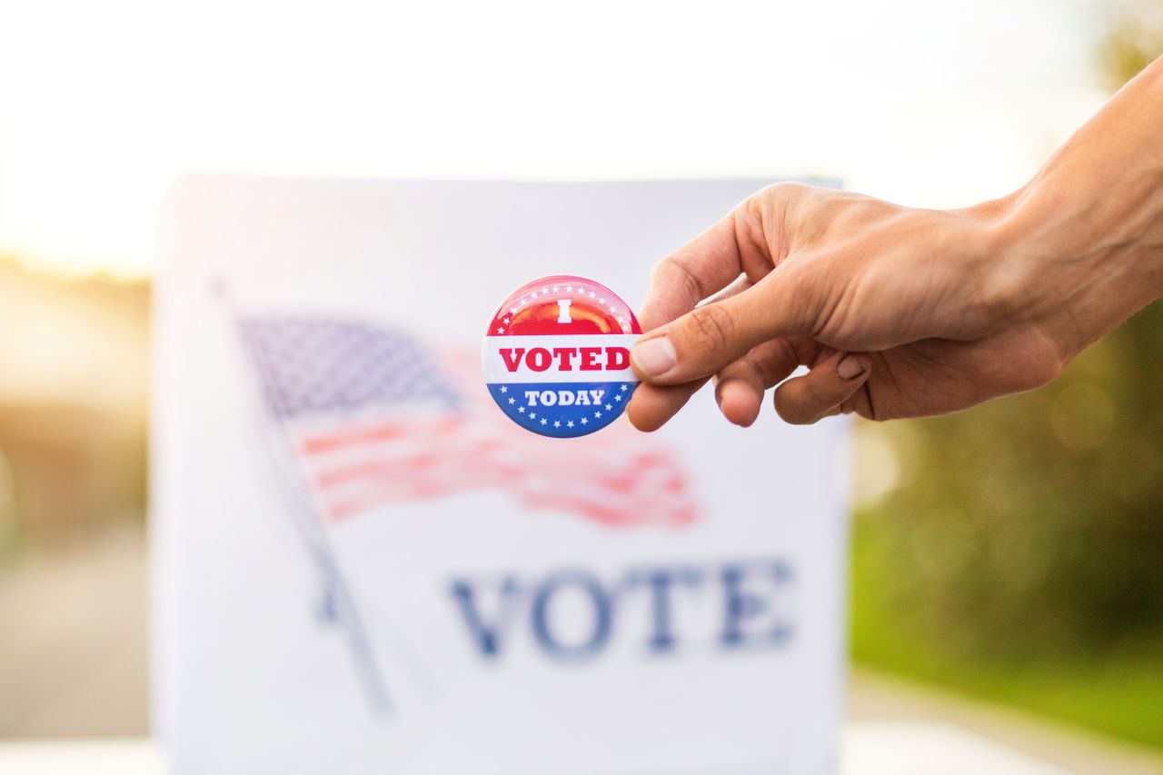 Hand holding voting pin in front of voting sign