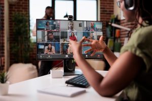 African American presenter working virtually gesturing in video conference with colleagues at desk.
