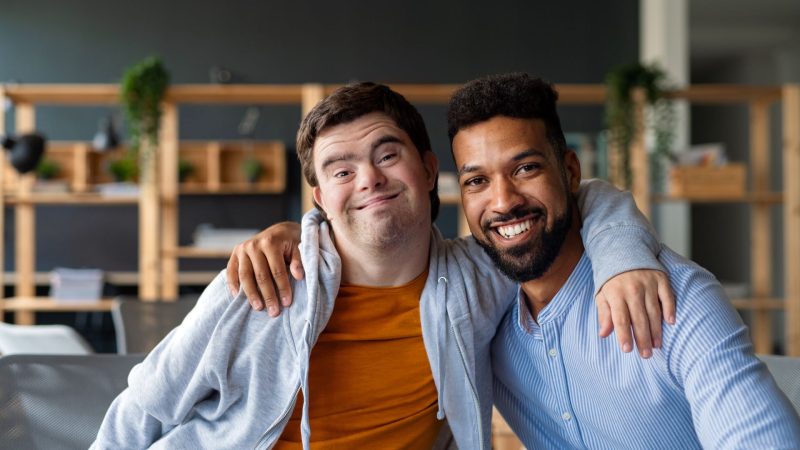 Two men with disabilities pose for a photo together with arms around each other