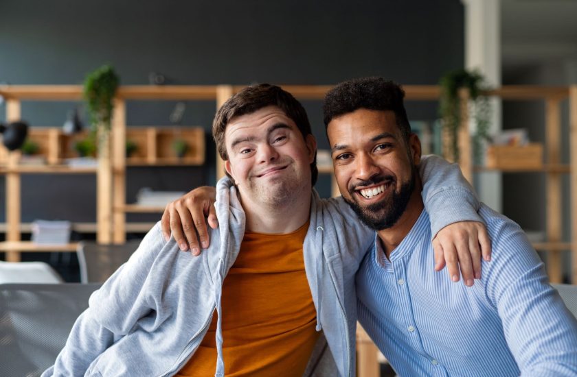 Two men with disabilities pose for a photo together with arms around each other