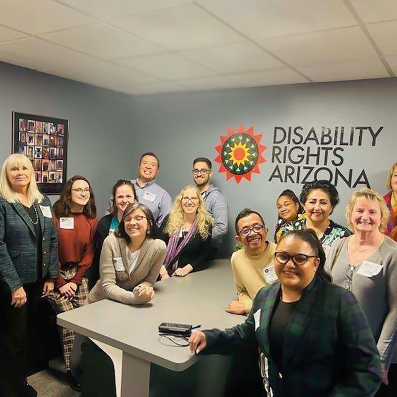 Disability Rights Arizona staff pose for a group photo in front of DRAZ logo