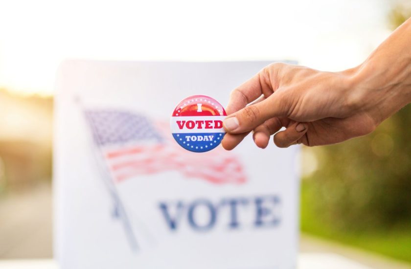 Hand holding voting pin in front of voting sign