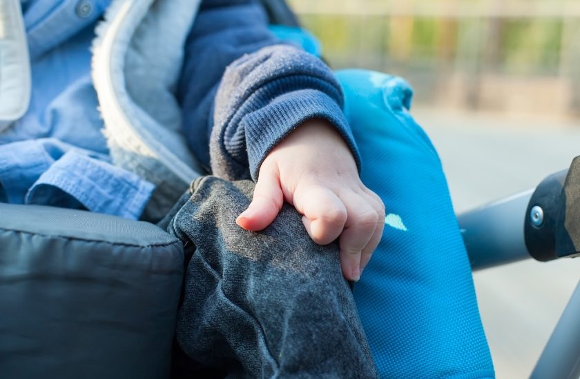 Close up photo of disable child sitting on the wheelchair in hospital walk way, His hand controlling the wheel