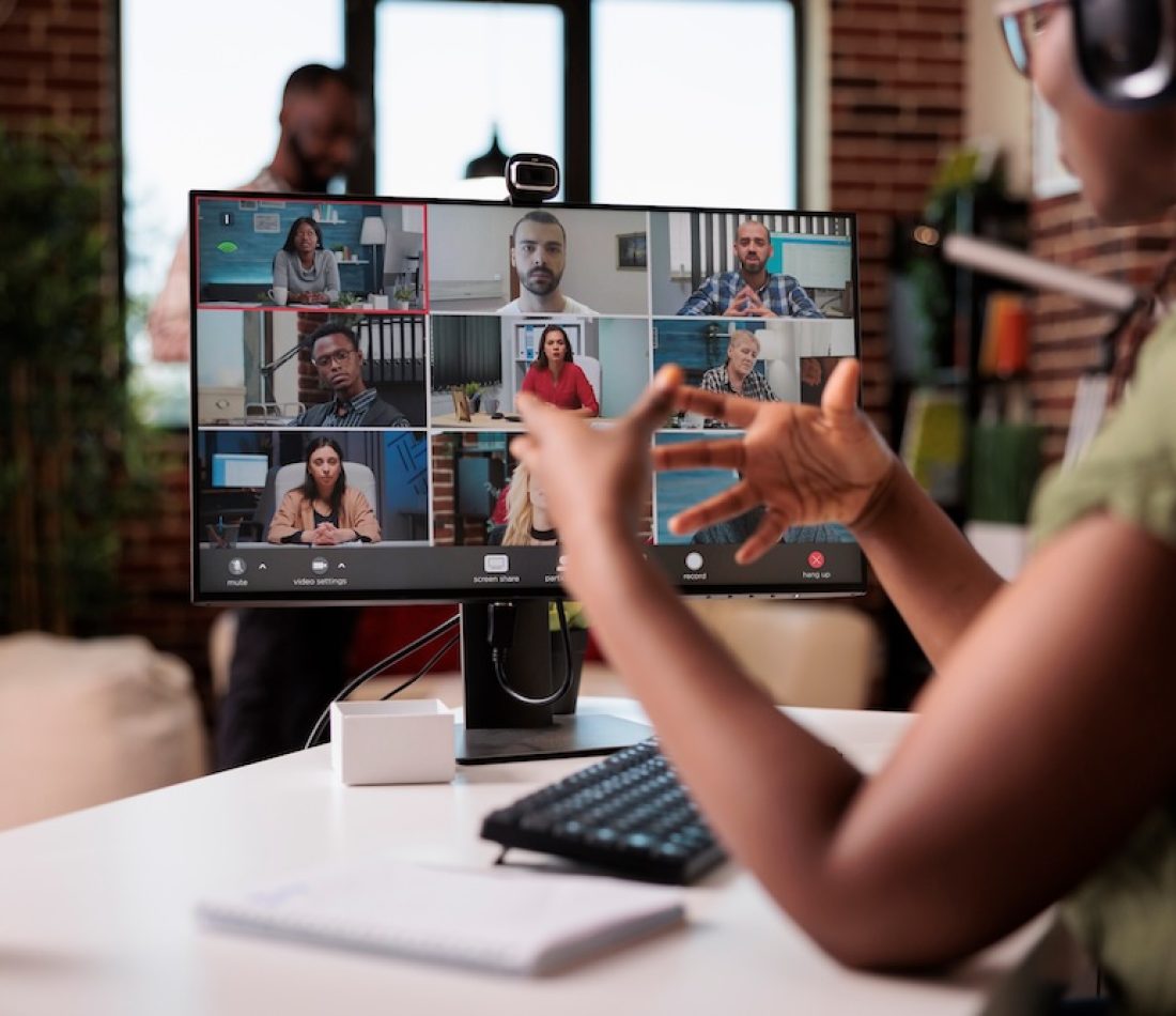 African American presenter working virtually gesturing in video conference with colleagues at desk.